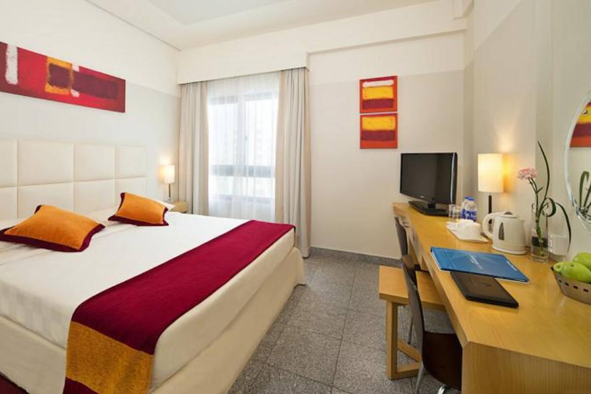 Une chambre d’hôtel avec un lit, un bureau, une télévision et une fenêtre avec des rideaux.