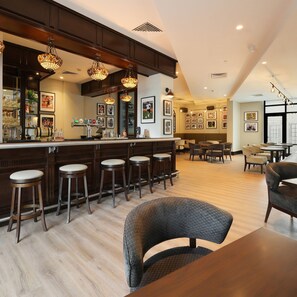 Un espace bar avec des tabourets en bois, un comptoir où sont disposés des verres et des bouteilles, et des tableaux encadrés accrochés au mur.
