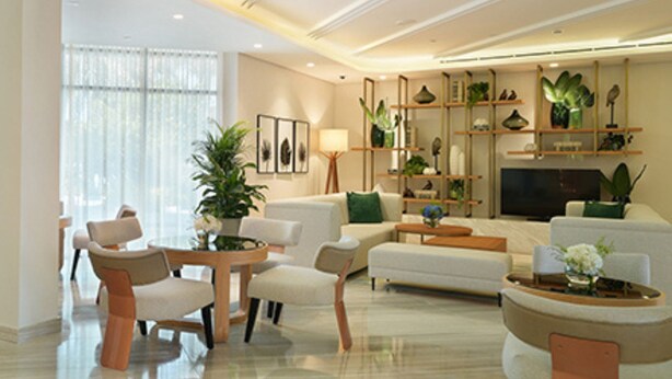 Un salon moderne avec un canapé, des fauteuils, une table basse et un téléviseur. Des plantes et des objets décoratifs sont disposés sur des étagères.
