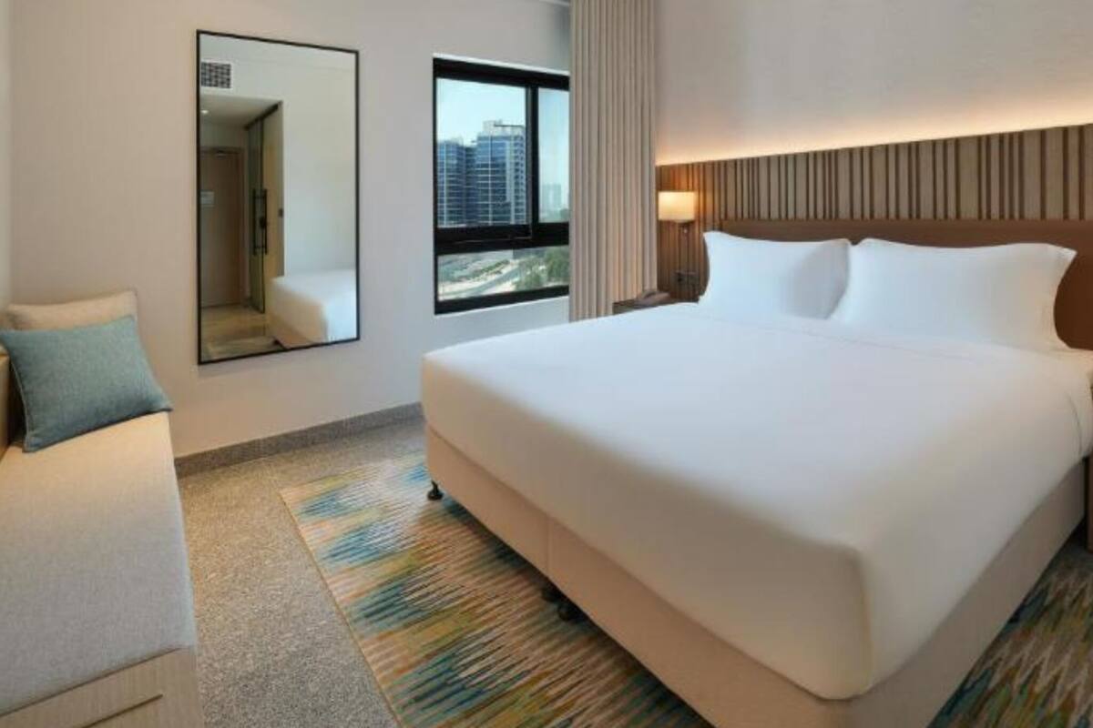 Une chambre d’hôtel avec un grand lit, un miroir, une fenêtre donnant sur la ville et un luminaire au plafond.