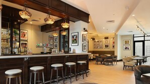 Un espace bar avec des tabourets en bois, un comptoir où sont disposés des verres et des bouteilles, et des tableaux encadrés accrochés au mur.