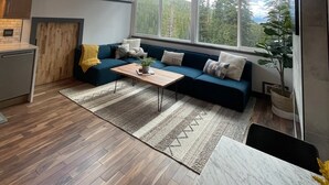 Un vaste espace de vie doté d’un plafond en bois, d’un canapé bleu, d’une table basse en bois et de grandes fenêtres offrant une vue sur l’extérieur.