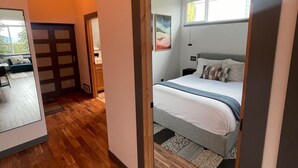 Une chambre à coucher moderne avec un plancher en bois, un lit recouvert de linge de lit blanc et un tableau accroché au mur.