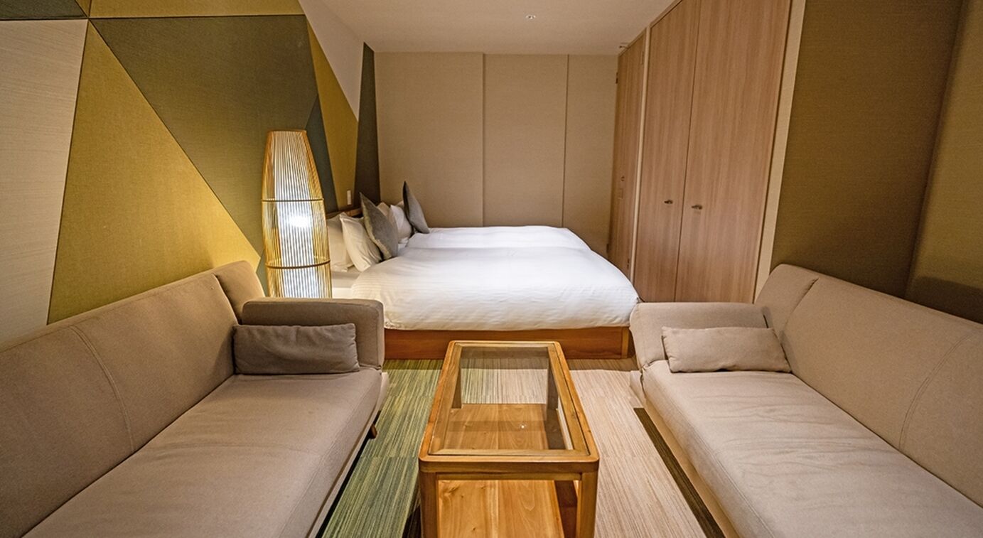 Une chambre d’hôtel avec un lit, deux canapés, une table basse en bois et une lampe.
