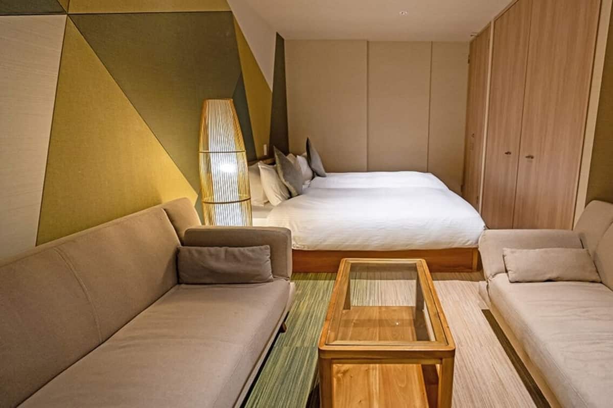 A hotel room with a bed, two sofas, a wooden coffee table, and a lamp.