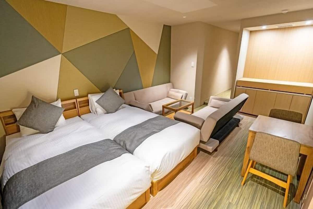 Ein Hotelzimmer mit zwei Betten, einem Sofa, einem kleinen Tisch und einem Fernseher.