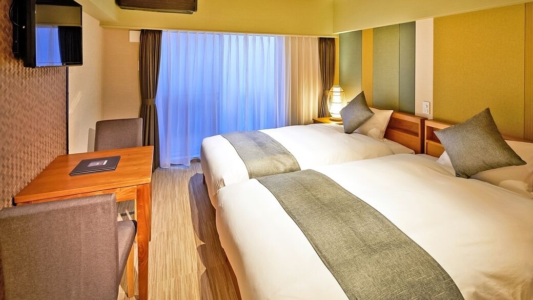 Une chambre d’hôtel avec deux lits, un bureau, une télévision et une fenêtre avec des rideaux.