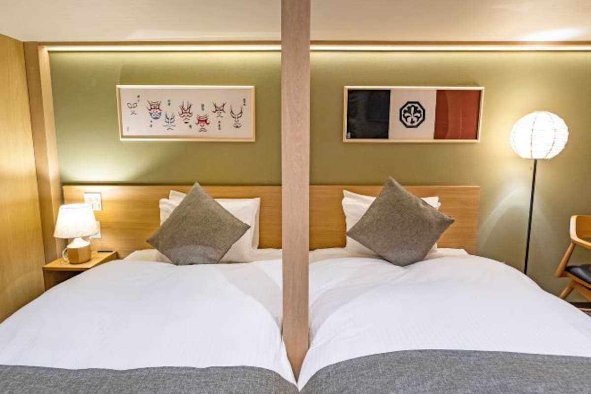 A double bed with two pillows, a nightstand with a lamp, and artwork on the wall.