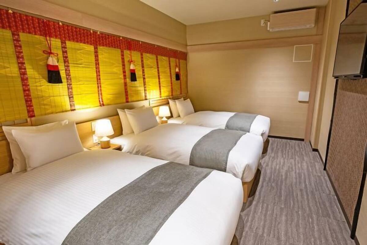 Ein Hotelzimmer mit zwei Betten, einem Kopfteil mit dekorativen Verzierungen, einem Fernseher und einer Wand-Klimaanlage.