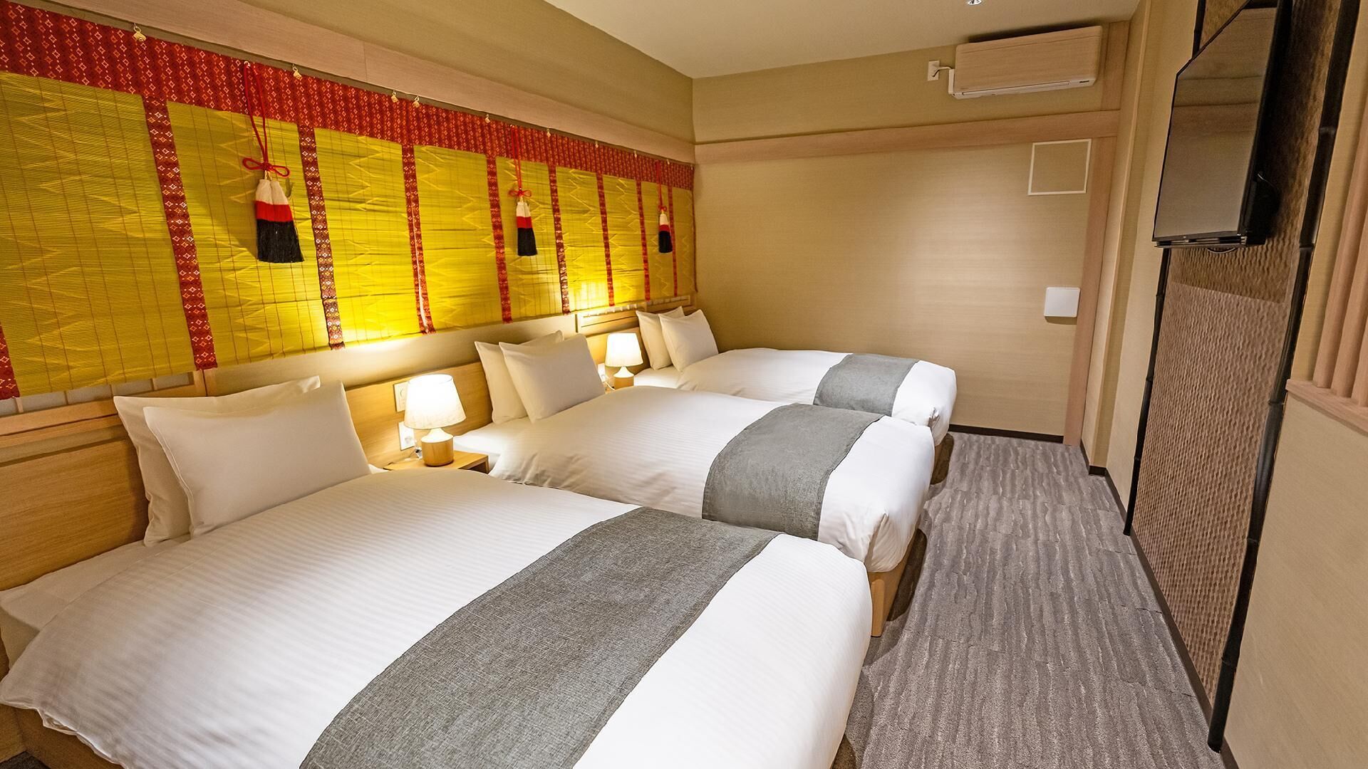 Une chambre d’hôtel avec deux lits, une tête de lit ornée d’un panneau décoratif, des lampes de chevet et un téléviseur.