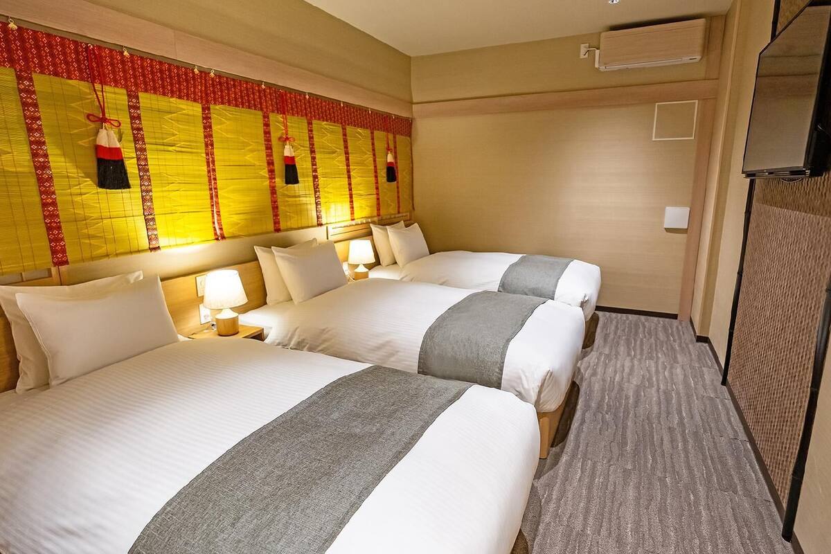 Ein Hotelzimmer mit zwei Betten, einem Kopfteil mit dekorativer Verkleidung, Nachttischlampen und einem Fernseher.