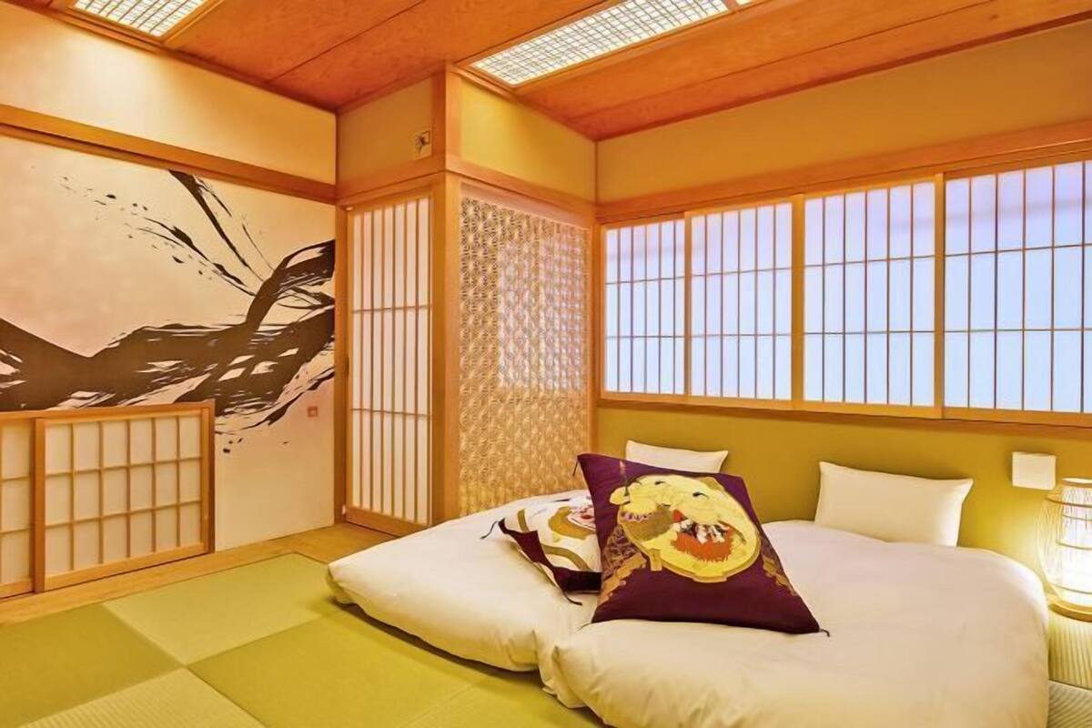 Ein traditioneller japanischer Raum mit Tatami-Böden, Shoji-Bildschirmen und einem Bett mit Zierkissen.