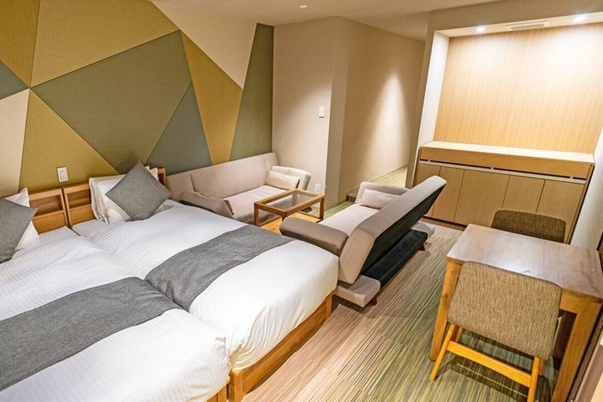 Ein Hotelzimmer mit zwei Betten, einem Schlafsofa, einem kleinen Tisch und einem Sessel.