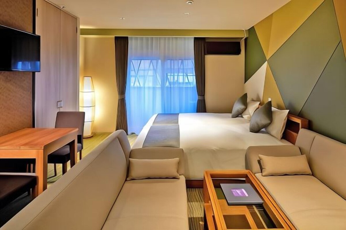 A hotel room with a bed, two sofas, a desk, and a TV.