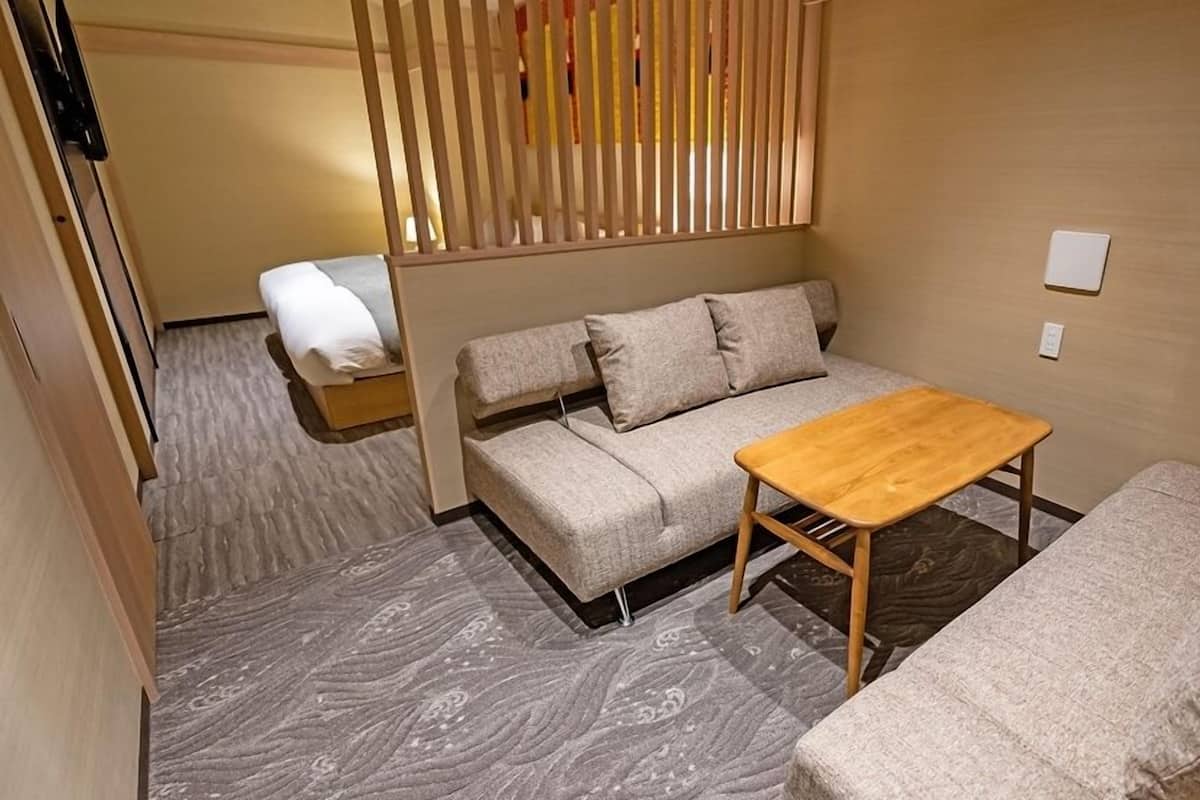 A compact room with a sofa, a small wooden table, and a bed.