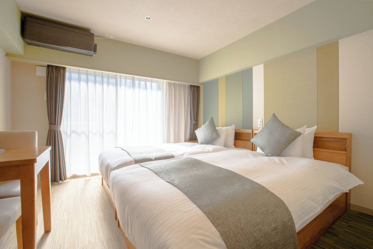 Ein Hotelzimmer mit zwei Betten, einem Schreibtisch und einem Fenster mit Vorhängen.