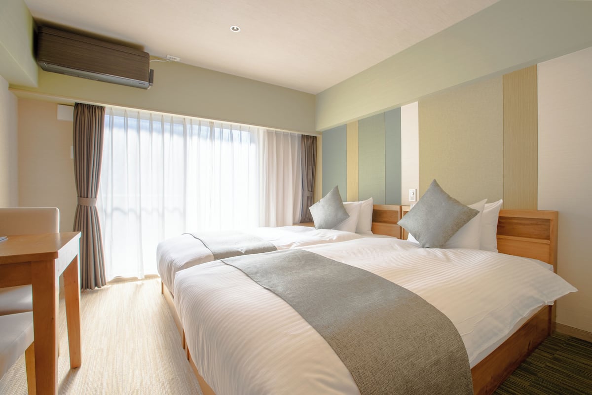 A hotel room with two beds, a desk, and a window with curtains.