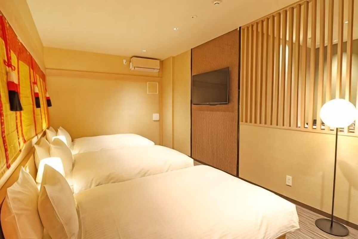 A hotel room with two beds, a TV, a lamp, and a wall-mounted air conditioner.