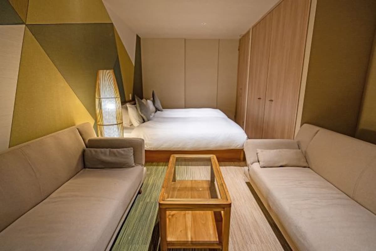 A modern hotel room with a large bed, two sofas, a wooden coffee table, and a geometric-patterned wall.