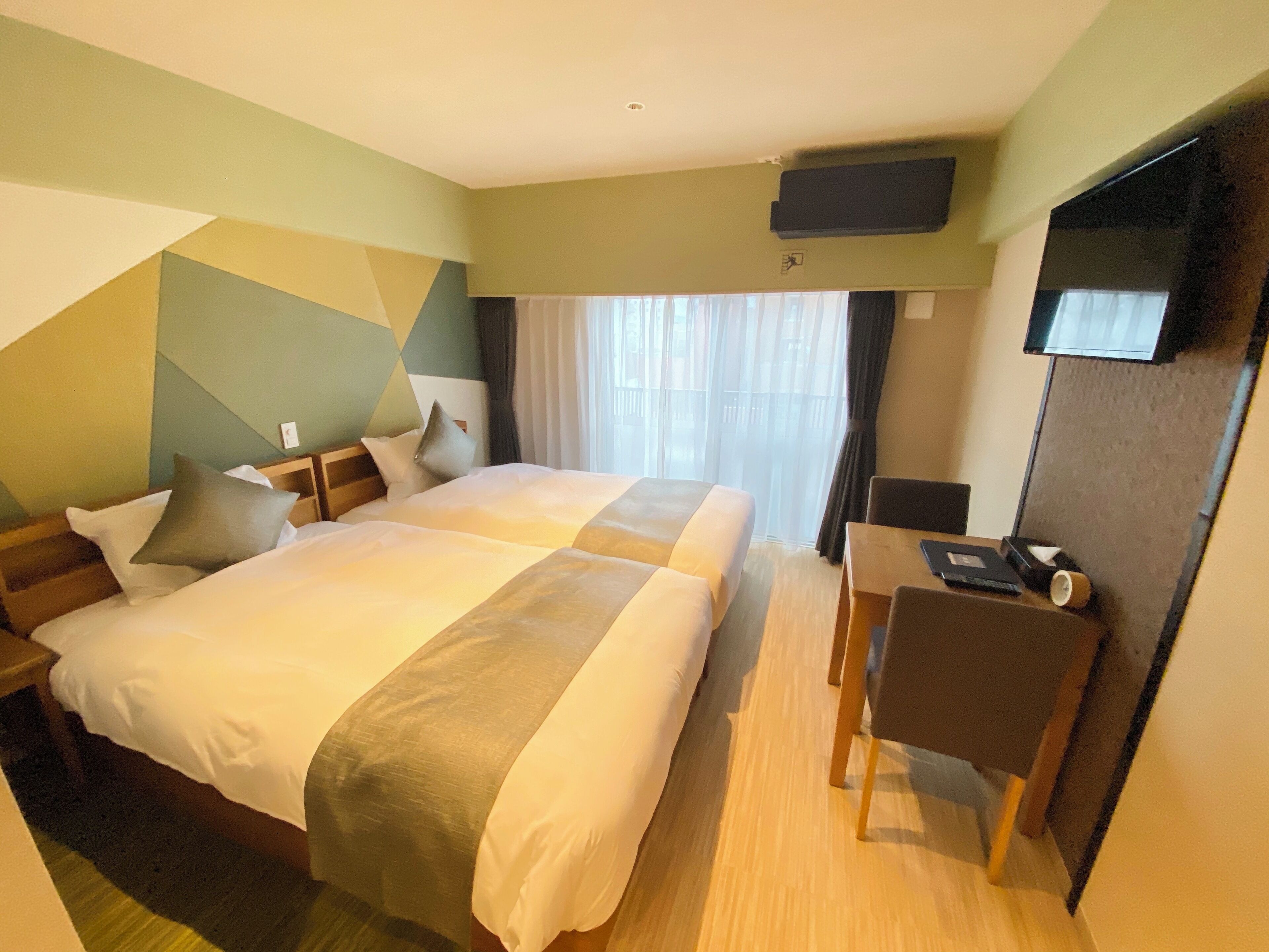 Une chambre d’hôtel avec deux lits, un bureau, une chaise, une télévision et une fenêtre avec des rideaux.