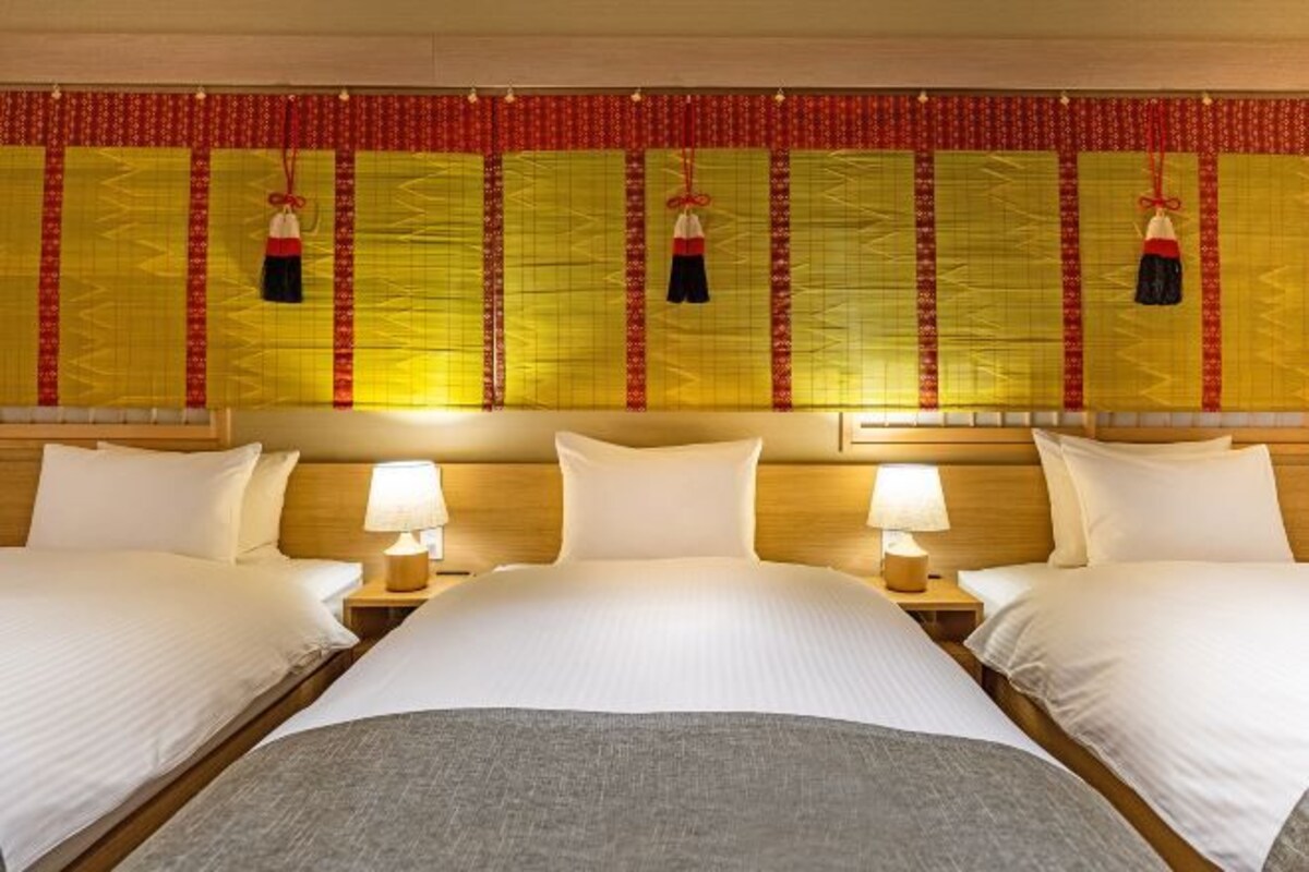 A hotel room with two beds, a wooden headboard, bedside lamps, and a decorative curtain with tassels.