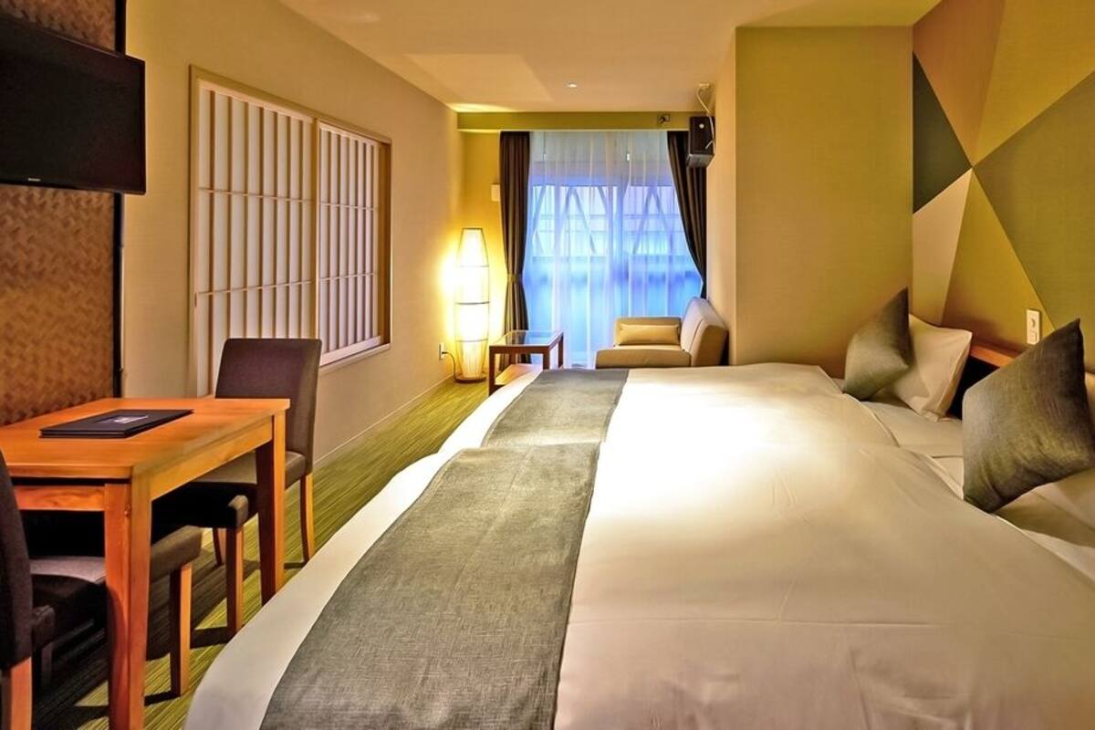 Ein Hotelzimmer mit Bett, Schreibtisch, Stuhl, Fernseher und einem Fenster mit Vorhängen.