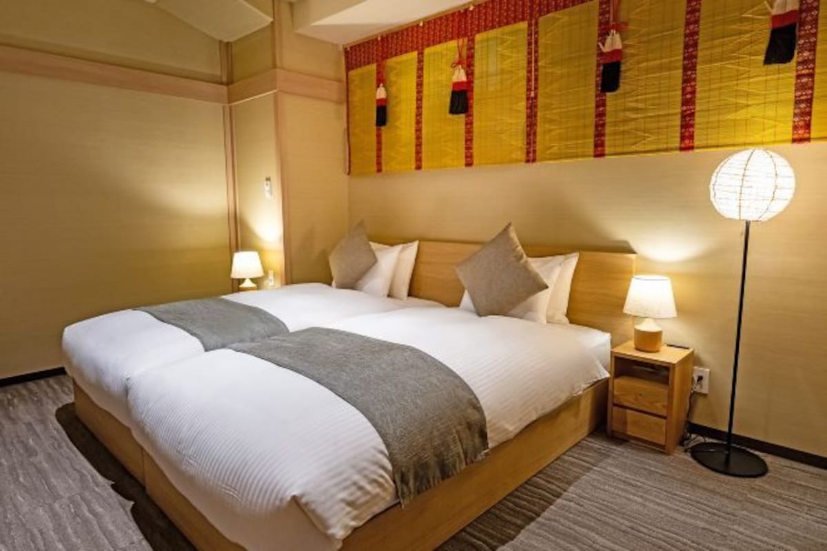A hotel room with a large bed, two bedside tables, a wall-mounted lamp, and a patterned wall hanging.