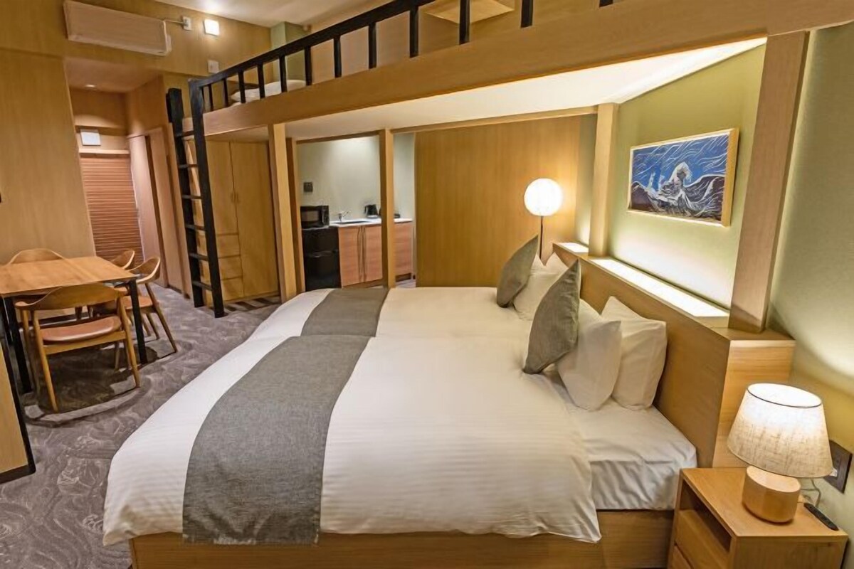 A bedroom with a bunk bed, a desk, and a chair, a bedside table with a lamp, and a painting on the wall.