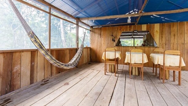 A wooden cabin with a hammock, a dining area with tables and chairs, and a view of the forest. - Red Uakari Jungle Lodge (Iquitos)