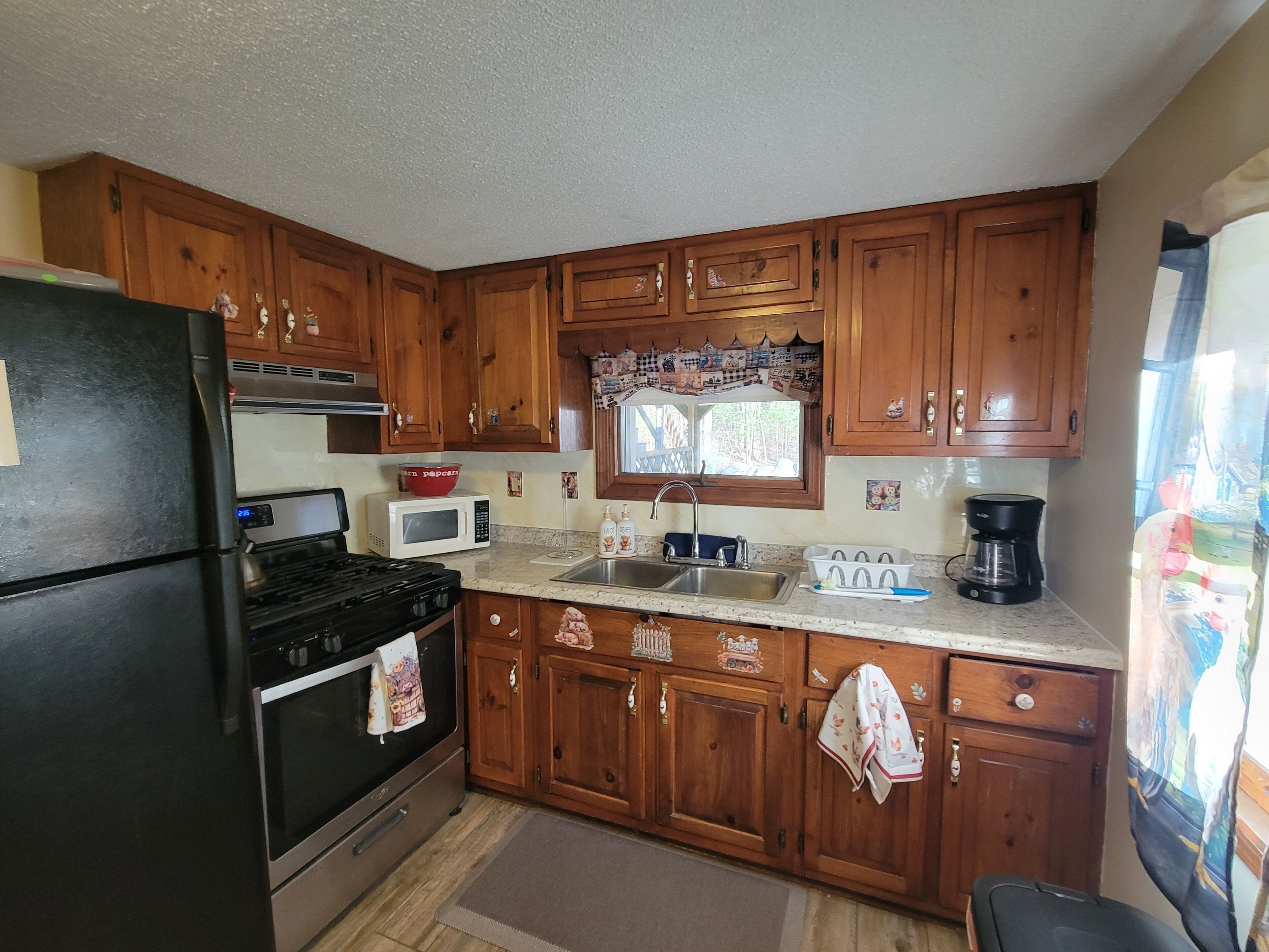 A kitchen with wooden cabinets, a black refrigerator, a microwave, a stove, and a coffee maker.