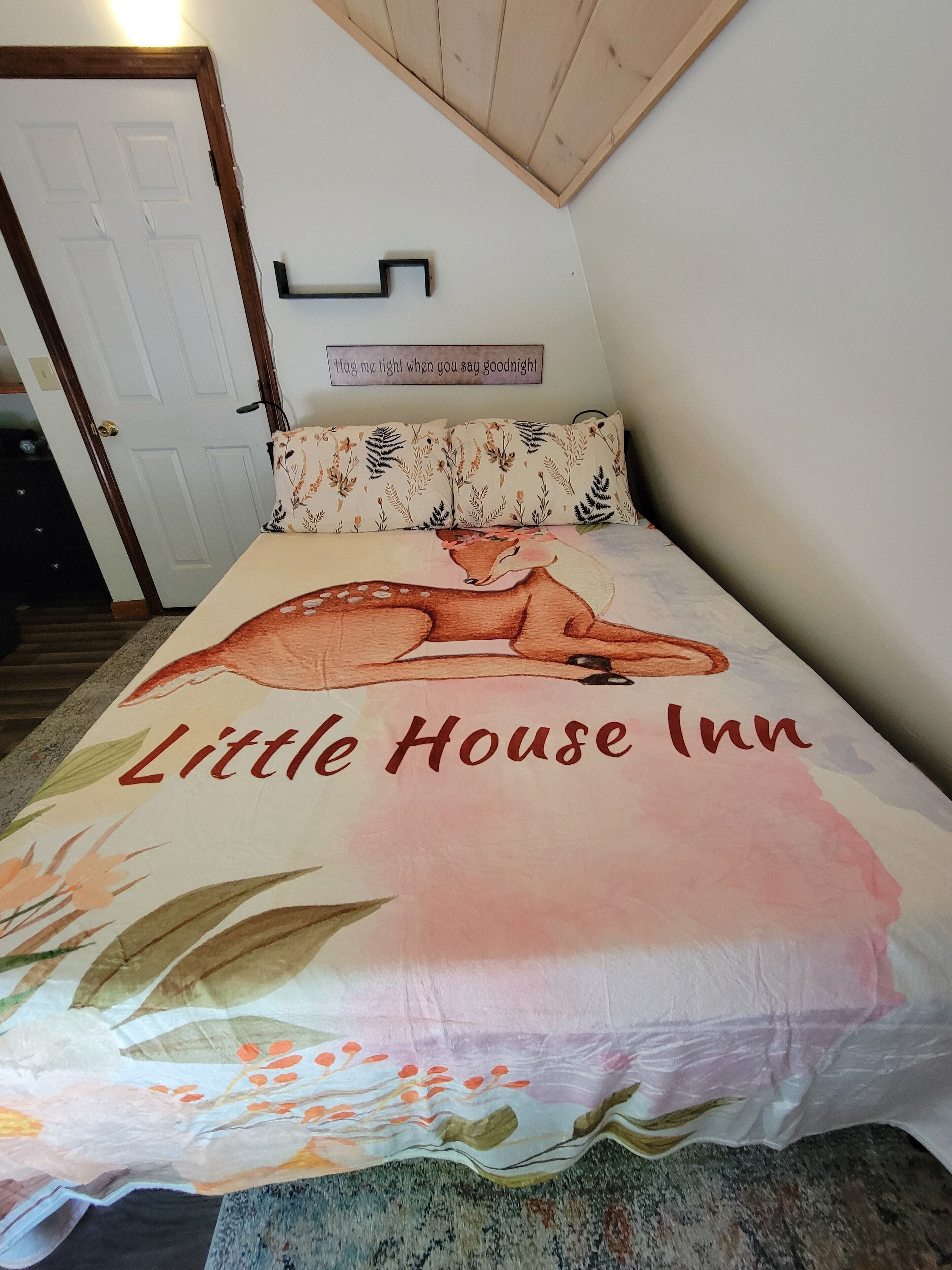 Una cama con estampado floral y el texto 'Little House Inn' en la colcha.