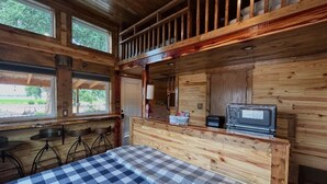 Een knus logies in houten stijl met een bed, een klein kitchenette, een televisie en een balkon met een hekwerk.