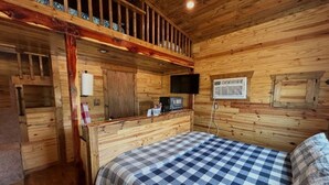 Een knus kamer in chaletstijl met houten inrichting, een bed met ruitjesdeken, een televisie en een klein raam.