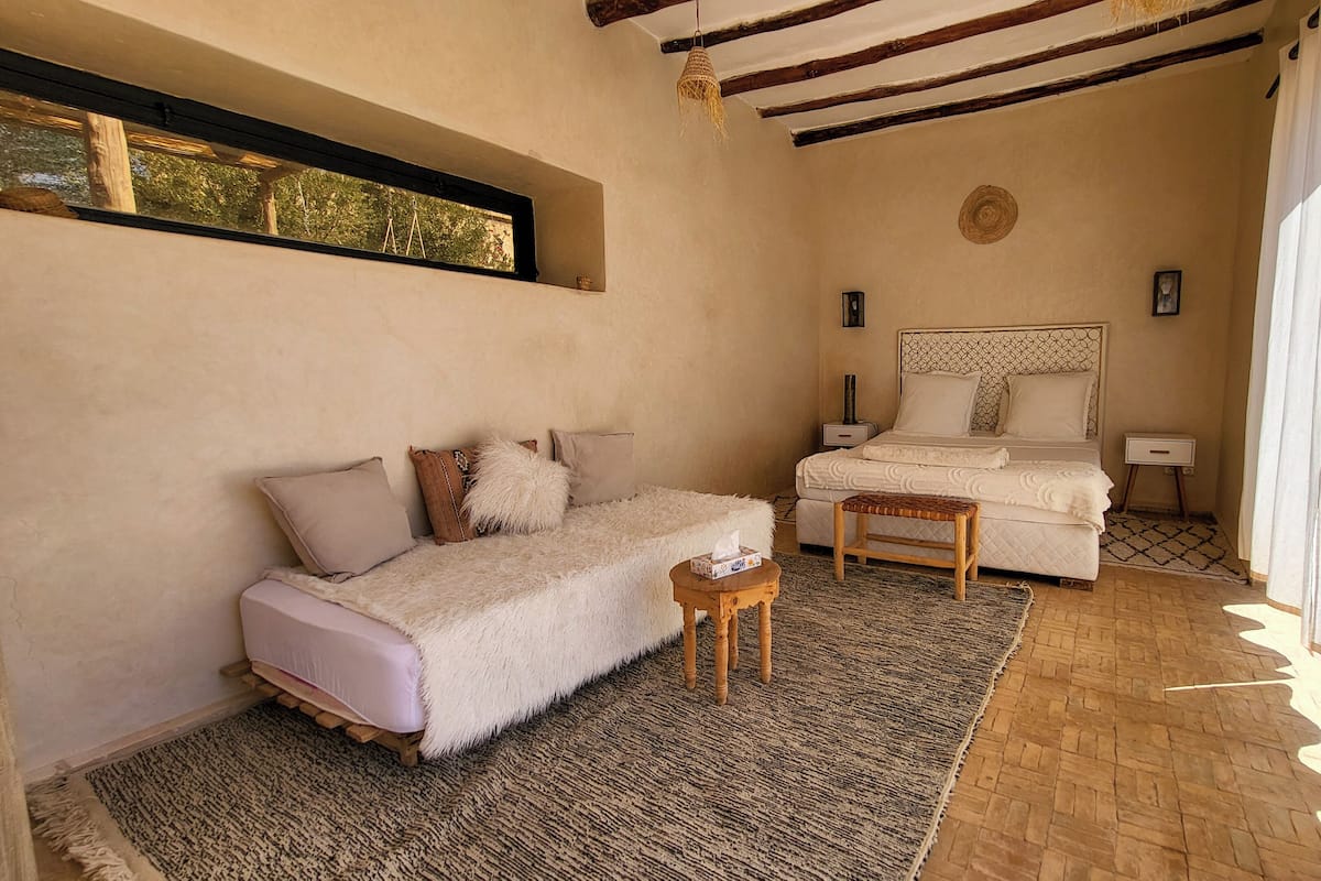 A cozy bedroom with a bed, a small table, a sofa, and a window with curtains.