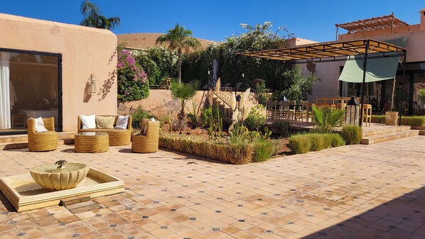 Un patio al aire libre con mobiliario de mimbre, una fuente de agua y una zona de estar cubierta.