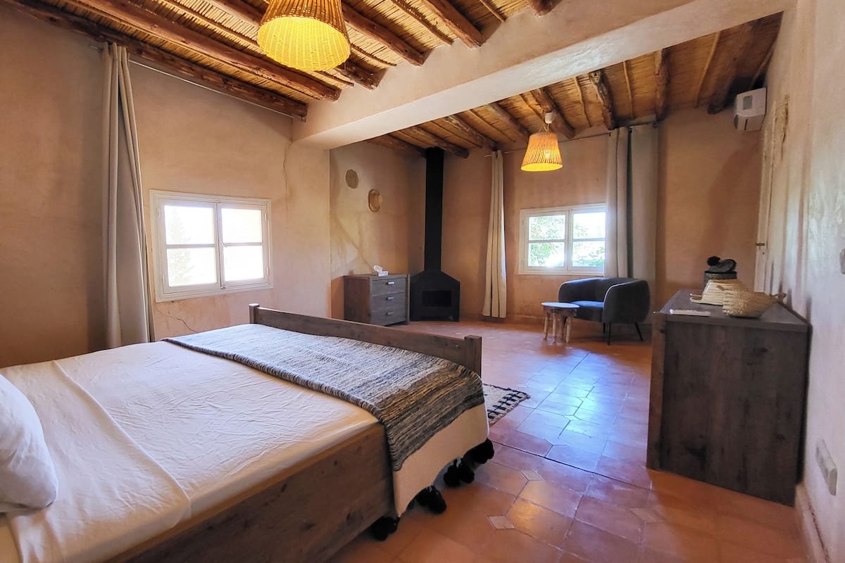 A bedroom with a bed, a dresser, a chair, a fireplace, and a window.