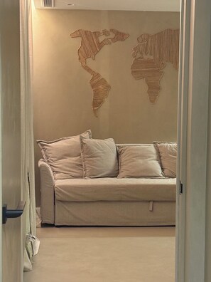 Una habitación con un sofá color beige y dos mapas del mundo en la pared.