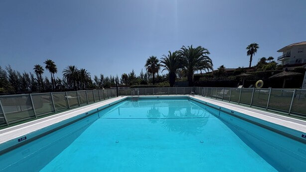 Piscina rectangular con agua azul cristalina, rodeada por una valla de metal.