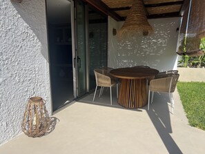 Un patio al aire libre con una mesa redonda de madera y cuatro sillas, una lámpara de mimbre y una puerta de cristal que da al interior.