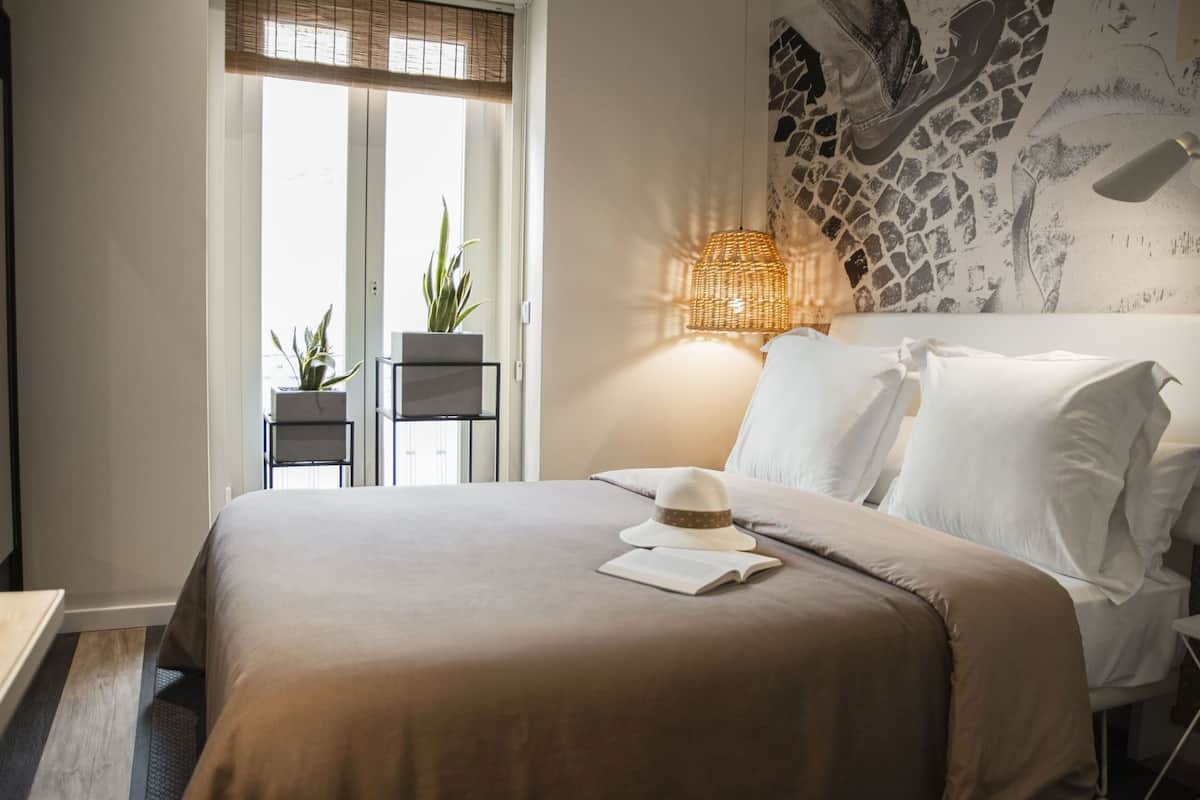 A neatly arranged bedroom with a bed, bedside lamps, and a window with blinds.