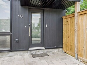 A modern building entrance with a dark facade, a wooden fence, and a numbered door.