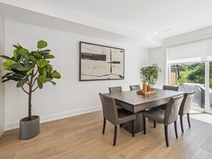 A modern dining area with a wooden table, six chairs, a potted plant, and a large abstract painting on the wall. - Luxury Resort Villa in Muskoka (Gravenhurst)
