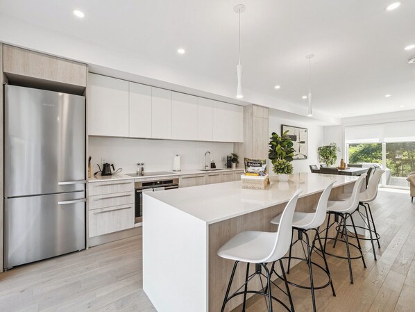 A modern kitchen with a large island, stainless steel appliances, and a view to the outside.