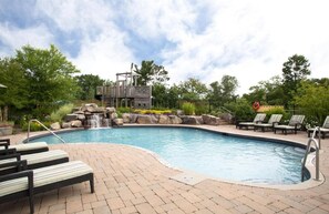 A swimming pool with a waterfall feature, lounge chairs, and a deck area.