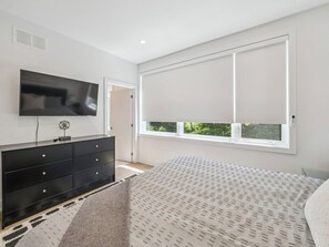 A bedroom with a bed, a black dresser, a television, and a window with blinds. - Luxury Resort Villa in Muskoka (Gravenhurst)