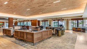 Eine geräumige Lobby mit Empfangstresen, Sitzgelegenheiten und großen Fenstern mit Blick auf Palmen.