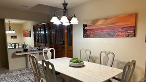 Un coin repas avec une table et des chaises en bois, un lustre et un tableau représentant un paysage de canyon.