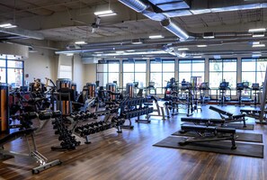A gym with various exercise equipment, large windows, and a wooden floor.