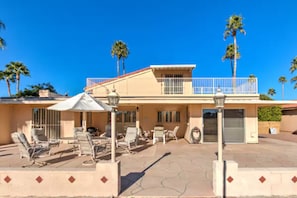 A two-story building with a balcony, outdoor seating, and palm trees.