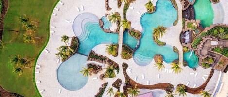 An aerial view of a resort with multiple swimming pools, palm trees, and lounge areas.